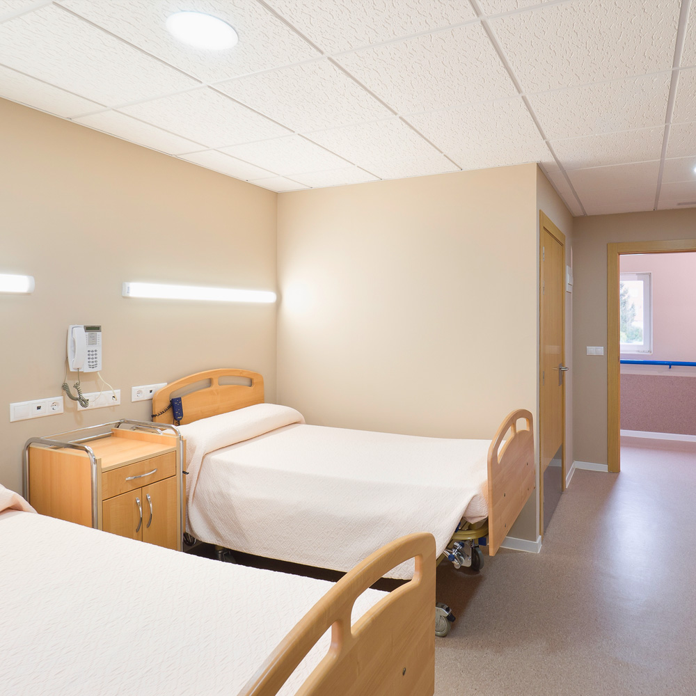 Vista de una habitación doble del centro residencial Baño Salud con dos camas, mesilla de noche y teléfono