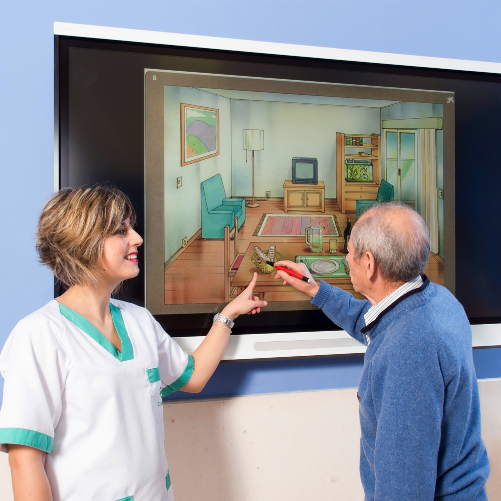Una trabajadora de la residencia ayuda a un residente a realizar una actividad en una pantalla táctil