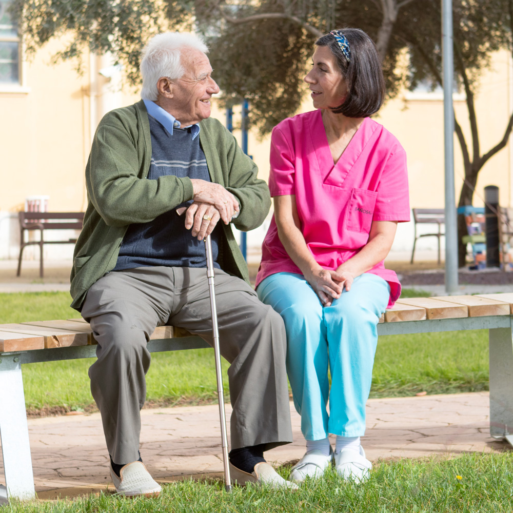 Trabajadora del centro residencial Baño Salud conversa con un residente en el patio exterior