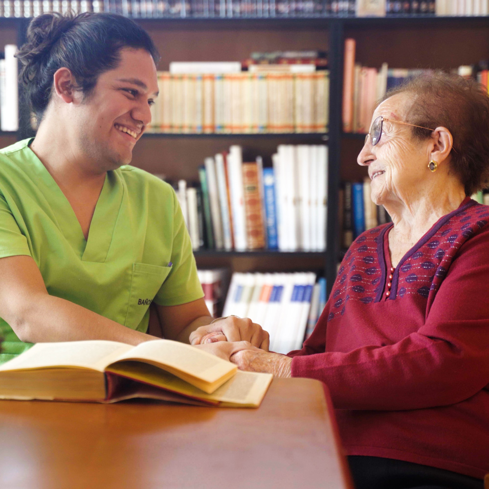 Un trabajador conversa con una residente en la biblioteca mientras leer un libro